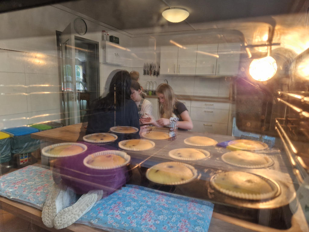 Ofen in dem sich Muffins befinden und Kindern die sich in der Ofenscheibe spiegeln während sie das Topping für die Muffins vorbereiten
