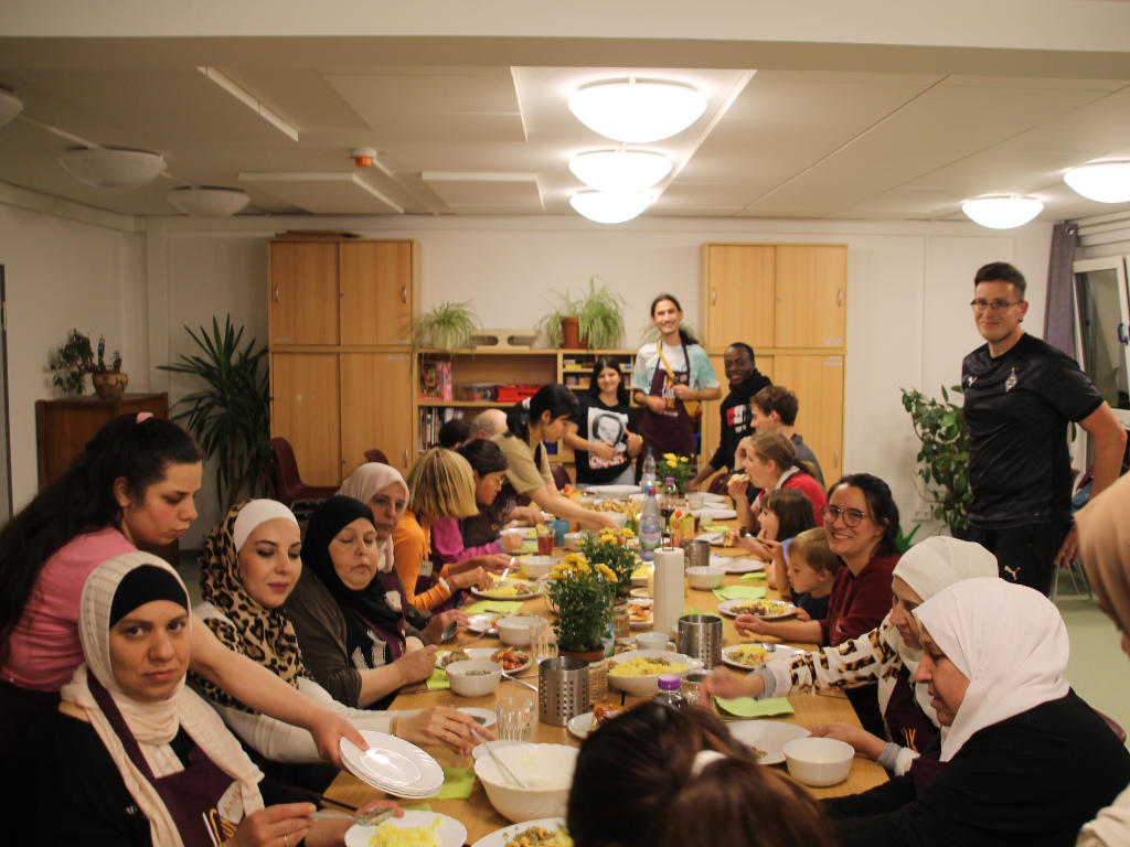 Eine Gruppe internationaler Kinder, Jugendlicher und Erwachsener beim Essen der verschiedenen Gerichte.
